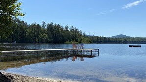 Un lago con un molo che si protende nell'acqua, circondato da alberi e una montagna in lontananza.
