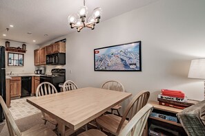 Un coin repas avec une table et des chaises en bois, un lustre et une cuisine en arrière-plan.