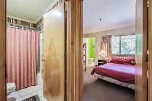 A room with a bed, a window, a bathroom with a shower curtain, and a door. - On Mountain two bedroom unit sleeping 6 (Newry)