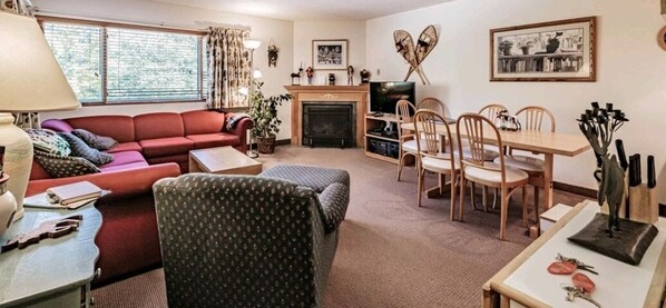 A cozy living room with a fireplace, a dining area with wooden chairs, and a sofa. - On Mountain two bedroom unit sleeping 6 (Newry)