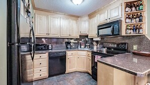 A kitchen with wooden cabinets, a black refrigerator, a microwave, a stove, and a shelf with bottles. - On Mountain two bedroom unit sleeping 6 (Newry)