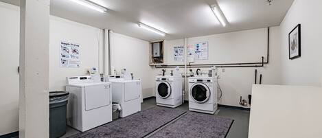 A laundry facility with four washing machines, a trash bin, and informational posters on the walls.