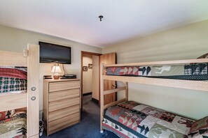 Quarto com beliche, escrivaninha, cadeira, televisão e porta que dá acesso a outro quarto.