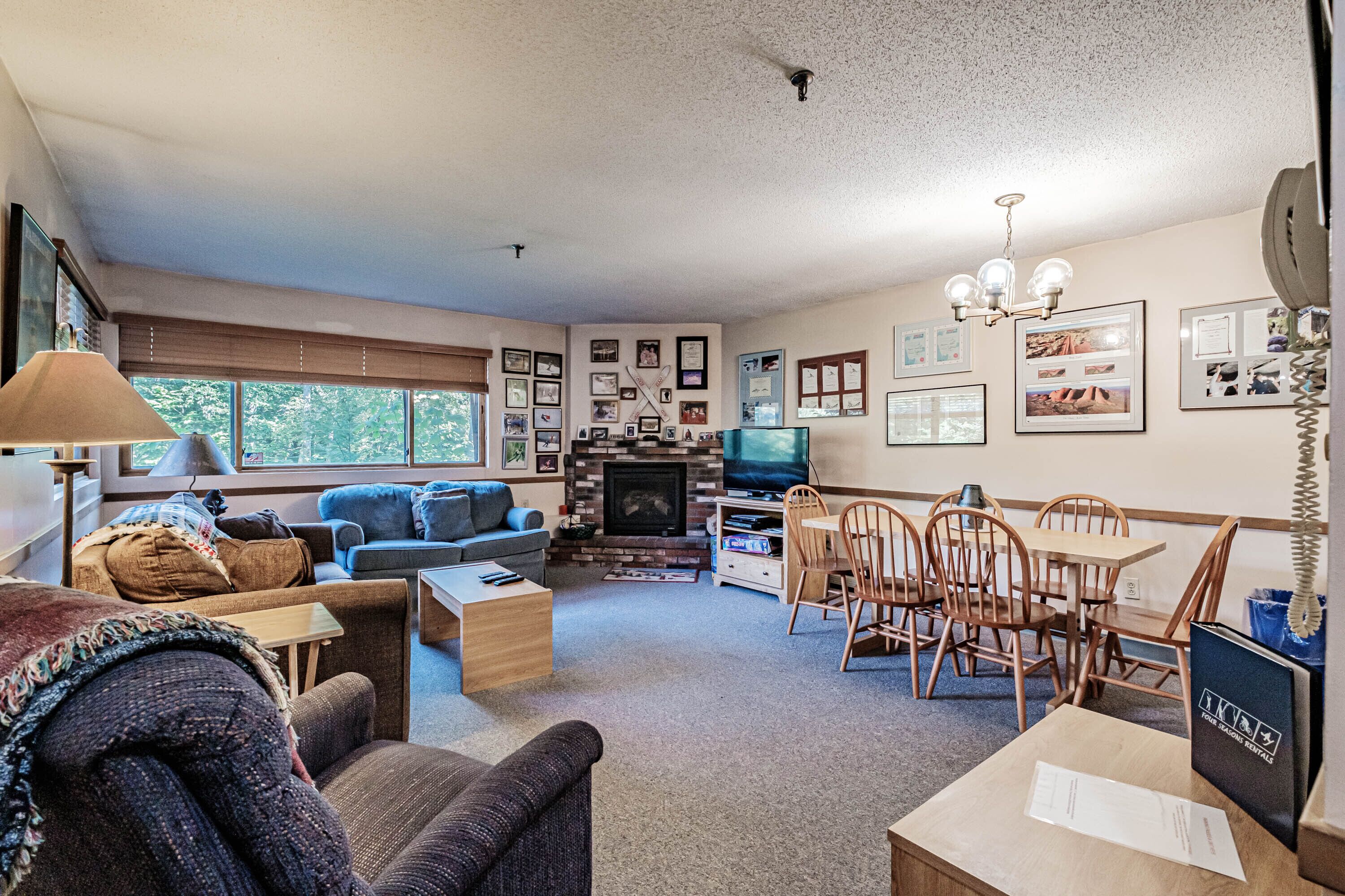 A cozy living room with a fireplace, a television, and a dining area with wooden chairs and a table.