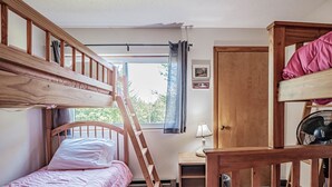 Une chambre de dortoir avec des lits superposés, un bureau, une chaise, une fenêtre avec des rideaux et une porte.