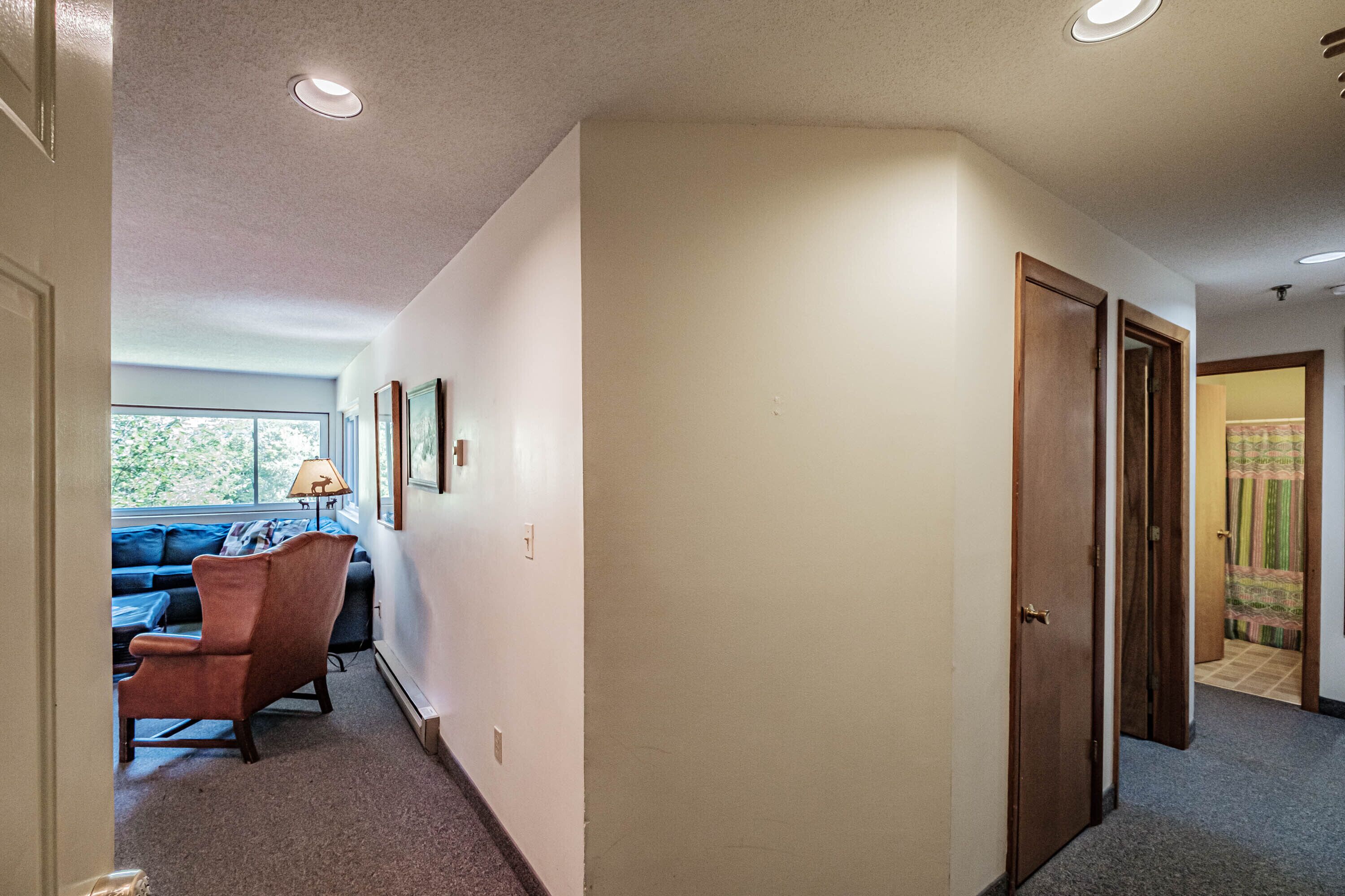 A hallway with a sofa, a chair, and a lamp. There are doors on the right and a window on the left.