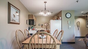 Un comedor con una mesa y sillas de madera, una araña, un refrigerador y un reloj en la pared.