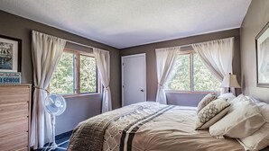 Un dormitorio con cama, ventilador, cómoda y ventana con cortinas.