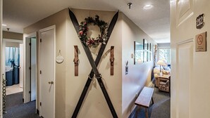 Un pasillo con un adorno decorativo en la pared, una puerta con el símbolo de número y una mesita con una lámpara.
