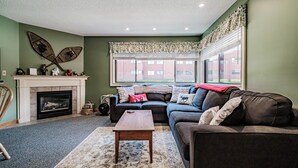 A living room with a fireplace, a sofa, a coffee table, and a large window with a view of a building. - On Mountain two bedroom unit sleeping 6 (Newry)