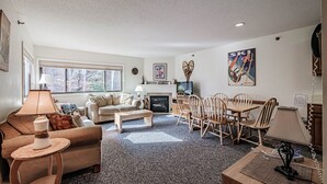 A cozy living room with a fireplace, a television, and a dining area with wooden chairs and a table. - On Mountain two bedroom unit sleeping 6 (Newry)