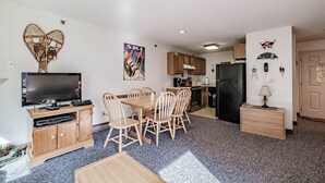 A living room with a TV, wooden dining table, and chairs, a kitchen with cabinets and appliances, and a small side table with a lamp. - On Mountain two bedroom unit sleeping 6 (Newry)
