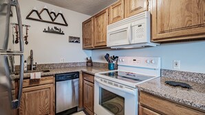 A kitchen with wooden cabinets, a white microwave, a stove, and a dishwasher. - On Mountain two bedroom unit sleeping 8 (Newry)
