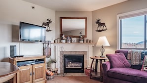 A living room with a fireplace, a television mounted above it, and a sofa. - On Mountain two bedroom unit sleeping 8 (Newry)