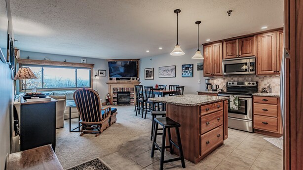 A spacious kitchen with wooden cabinets, a large island, and a dining area with chairs and a table. - On Mountain two bedroom unit sleeping 6 with air conditioning! (Newry)
