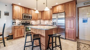 A modern kitchen with wooden cabinets, stainless steel appliances, and a central island with stools. - On Mountain two bedroom unit sleeping 6 with air conditioning! (Newry)