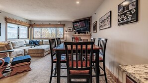 A cozy living room with a sofa, a dining table with chairs, a TV mounted on the wall, and a fireplace. - On Mountain two bedroom unit sleeping 6 with air conditioning! (Newry)