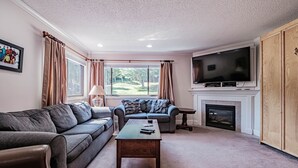 A living room with a sofa, a coffee table, a TV, and a fireplace. - North Peak 2-305 Ski-in Ski-out (Newry)