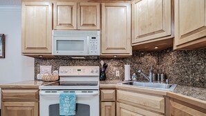 A kitchen with wooden cabinets, a microwave, stove, and granite countertop. - North Peak 2-305 Ski-in Ski-out (Newry)