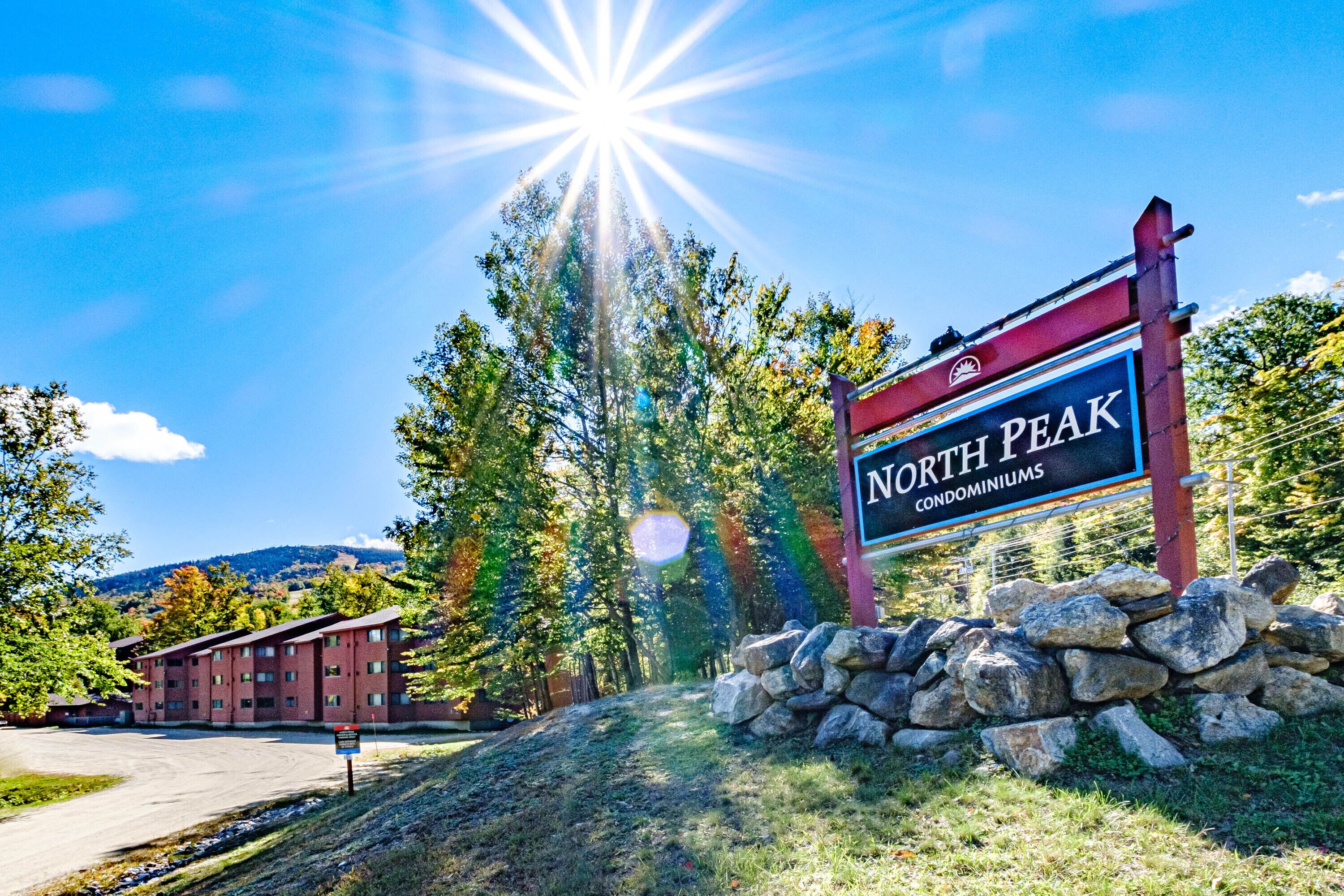 A sign for North Peak Condominiums with a stone wall and trees in the background.