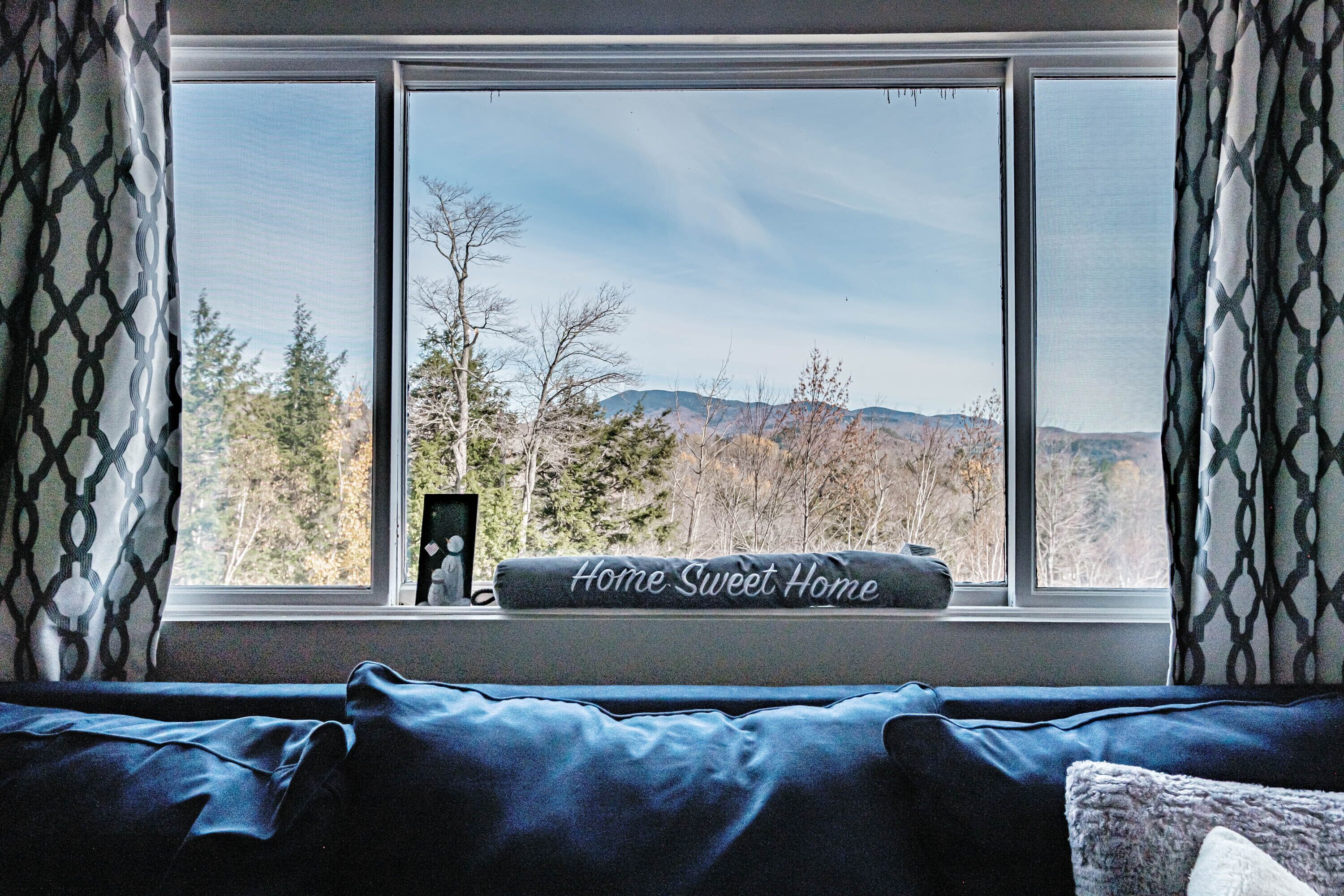 Un dormitorio con un ventanal grande, un edredón azul y una almohada con la inscripción 'Home Sweet Home'.
