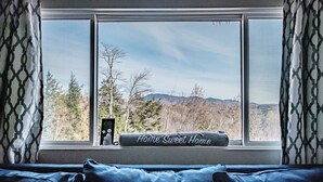 A bedroom with a large window, a blue bedspread, and a pillow with "Home Sweet Home" text.