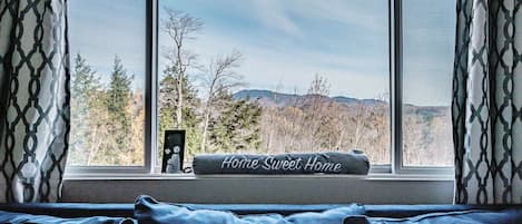 A bedroom with a large window, a blue bedspread, and a pillow with "Home Sweet Home" text.