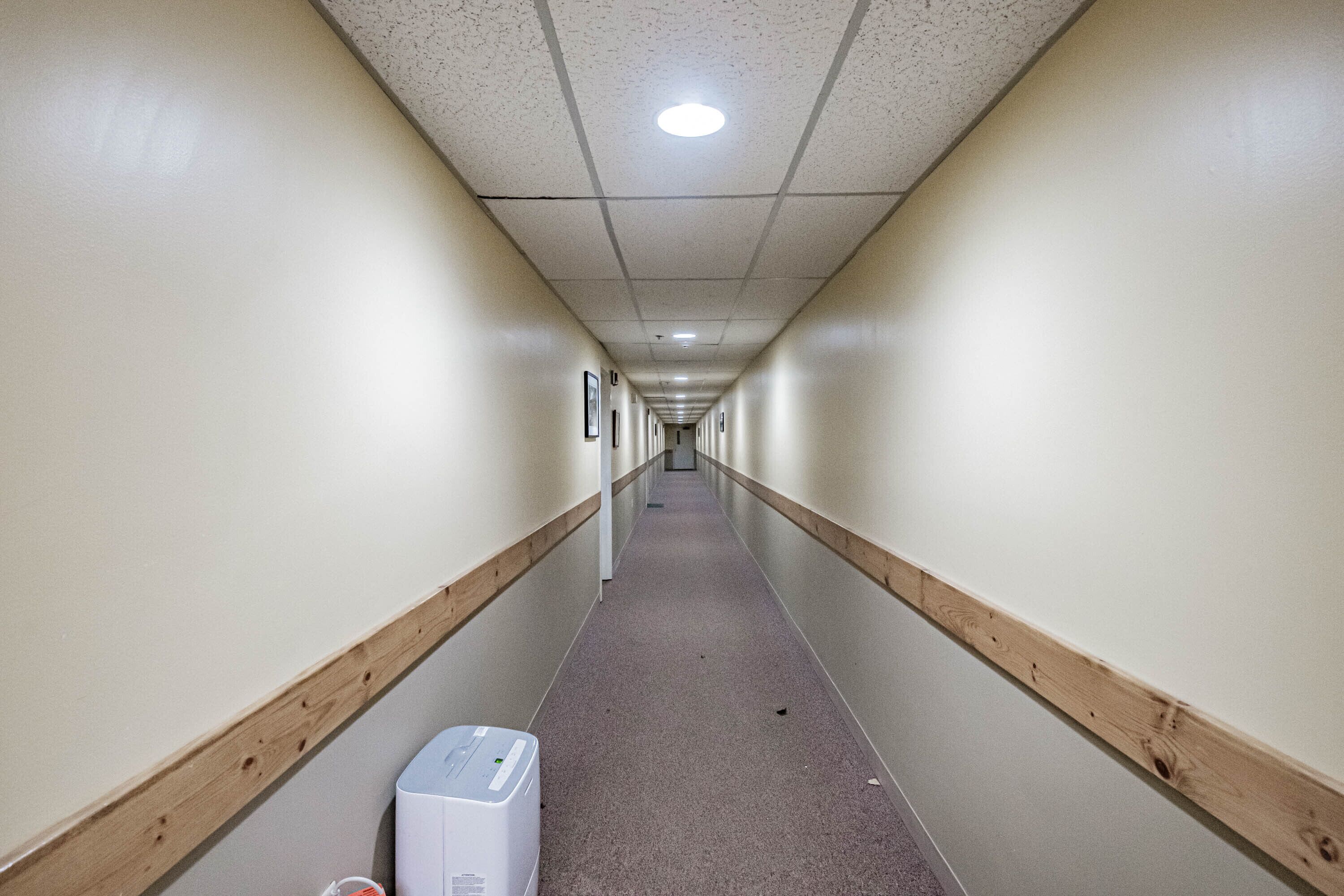 En lång, smal hall med träsocklar, en vit vägg och ett ljust golv.