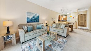 A living room with two sofas, a coffee table, and a TV. There is a kitchen in the background with a refrigerator and a microwave. - Cheerful Condo - minutes away from Disney/ with Pools, Resturant & Spa (Davenport)