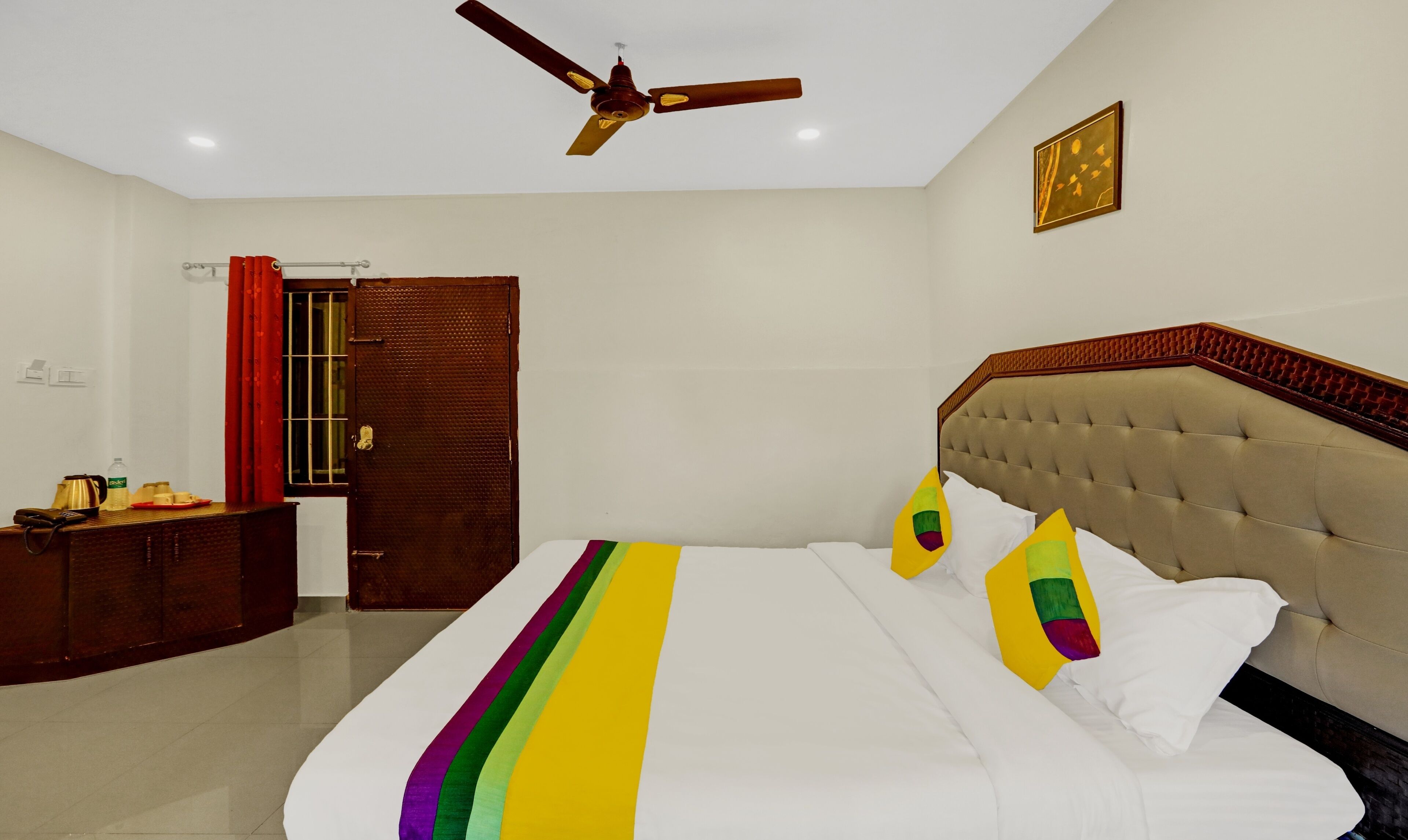 A bedroom with a bed, a ceiling fan, a door, and a nightstand.