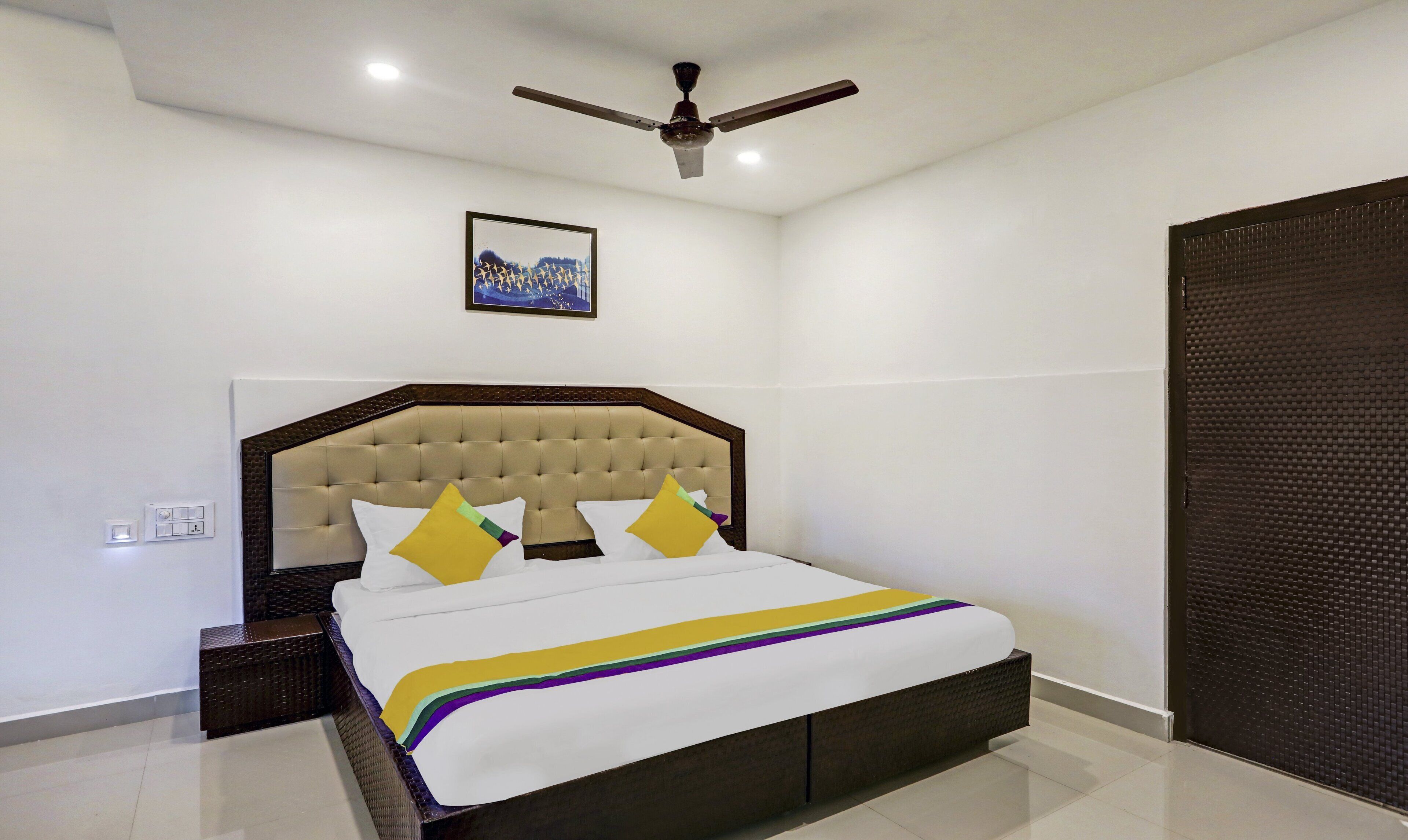 A neatly arranged bedroom with a large bed, a ceiling fan, and a framed picture on the wall.