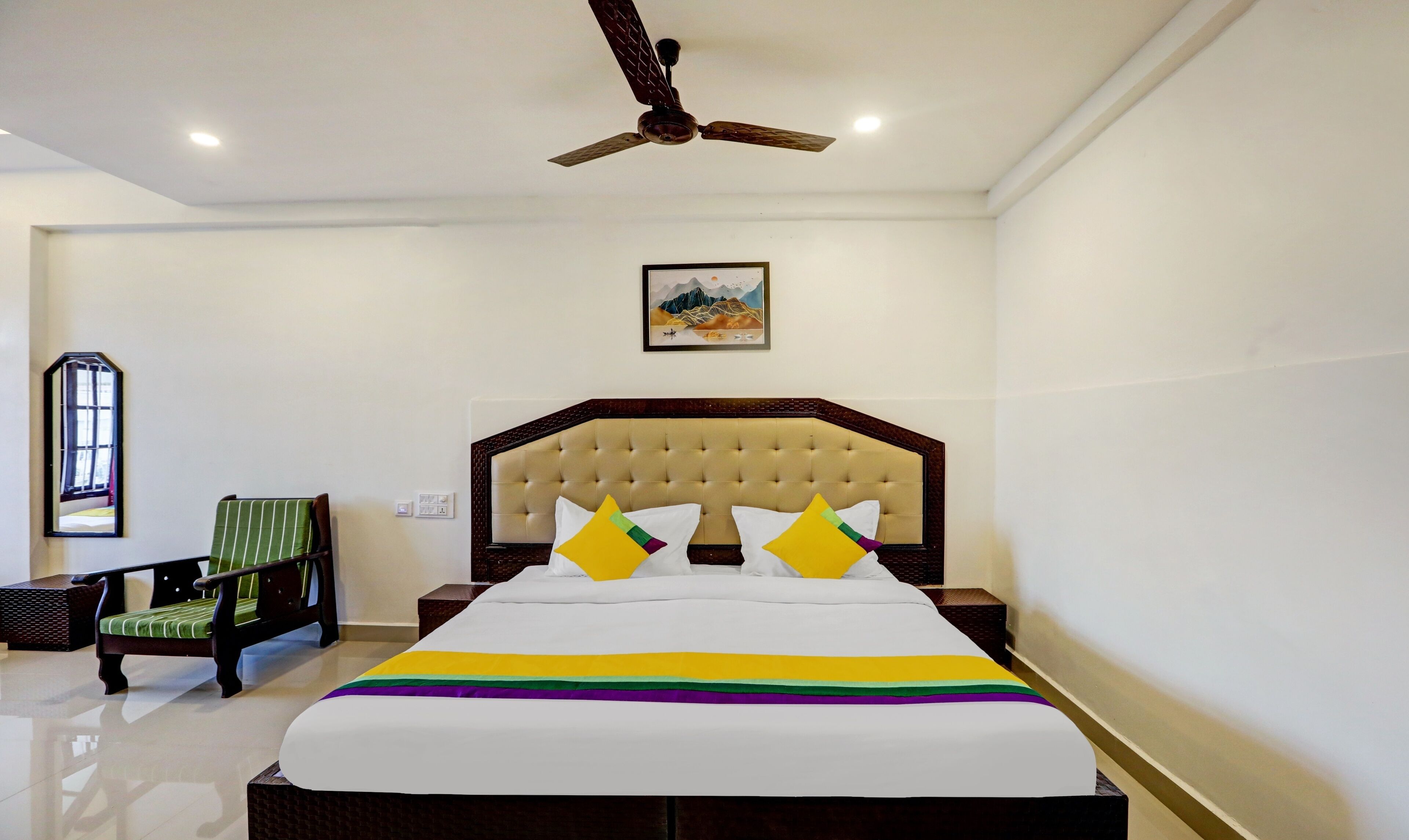 Een hotelkamer met een groot bed, een plafondventilator, een raam en een schilderij aan de muur.
