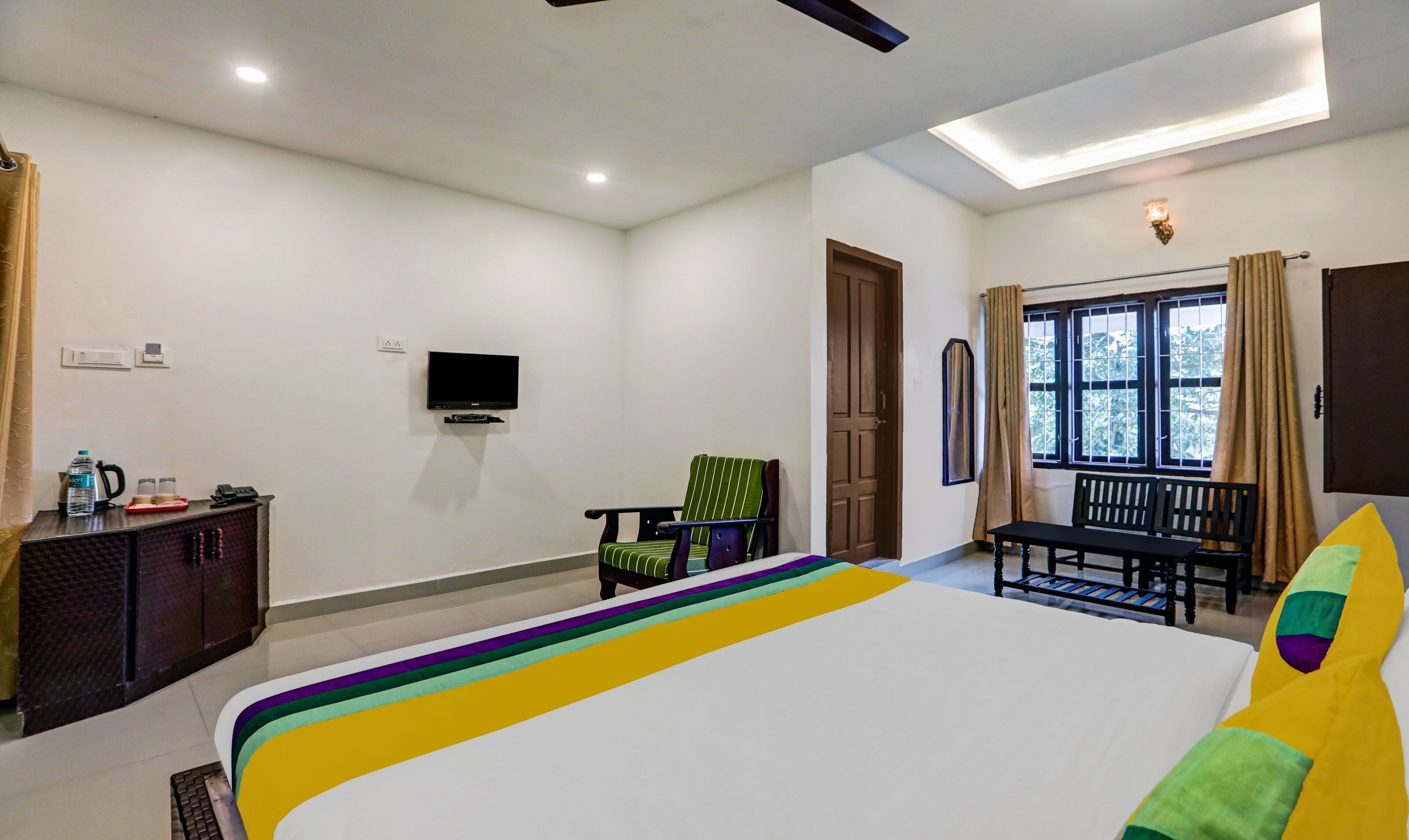 Une chambre d’hôtel avec un lit, un téléviseur fixé au mur, un bureau avec une chaise et une fenêtre avec des rideaux.