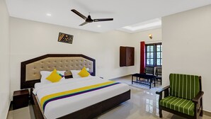 A hotel room with a large bed, a ceiling fan, a TV, a window with curtains, and a green chair. - Itsy Hotels Regalia Grand, 500 Mtrs From Madikeri Fort (Madikeri)