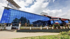 A modern hotel with a reflective glass facade, a prominent sign for the Hotel Regal, and a well-maintained garden area. - Itsy Hotels Regalia Grand, 500 Mtrs From Madikeri Fort (Madikeri)