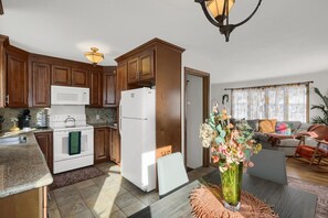 A kitchen with wooden cabinets, a white stove, and a refrigerator. There is a dining table with a vase of flowers.