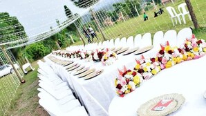 A long table set for a formal outdoor event with white tablecloths and floral centerpieces. - Beautiful woman hotel (Kampala)