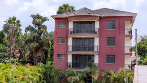 A multi-story hotel with balconies and large windows, surrounded by lush greenery. - Beautiful woman hotel (Kampala)