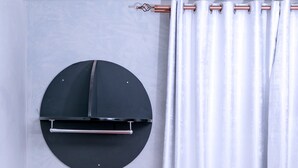 A room with a modern design, featuring a round black air conditioning unit on the wall, a red armchair, a matching ottoman, and a white curtain. - Beautiful woman hotel (Kampala)