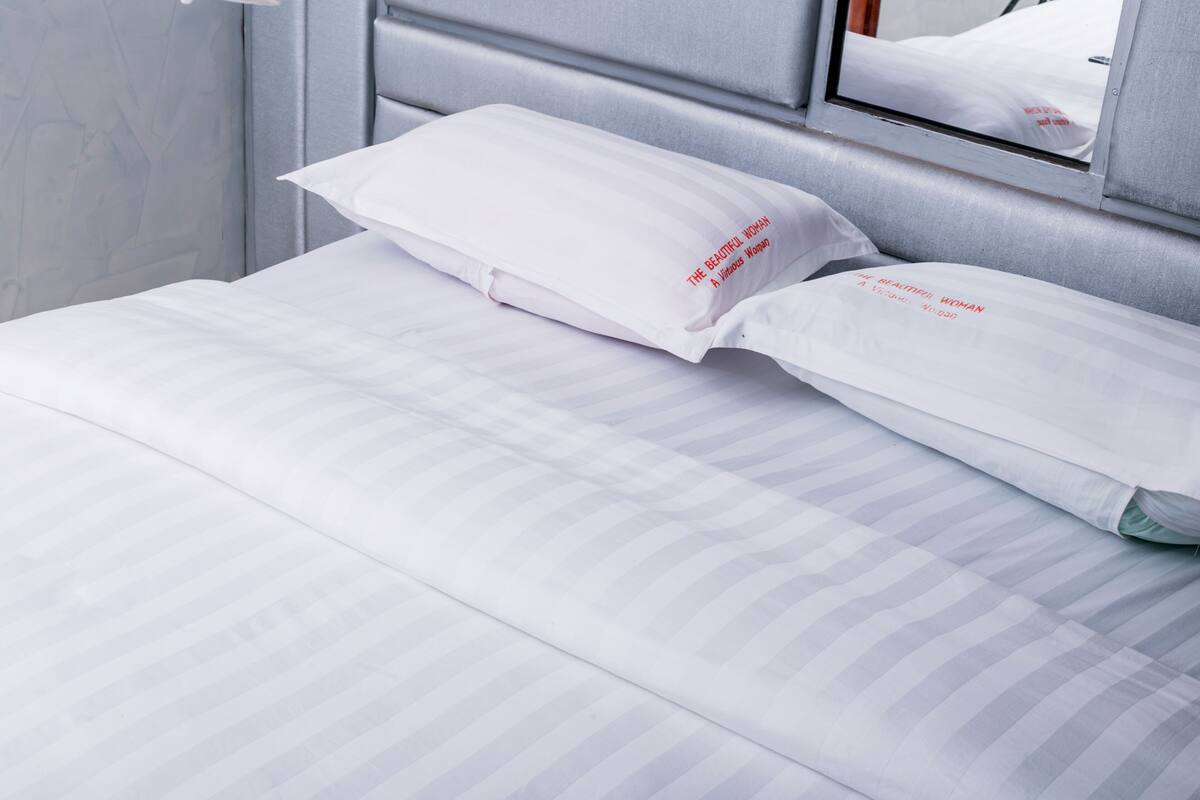 A neatly made bed with striped bedding and pillows with text on them.