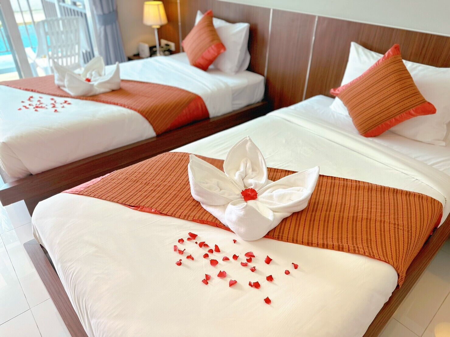 Zwei Hotelbetten mit weißen Laken, orangefarbenen Überwürfen und Zierkissen.