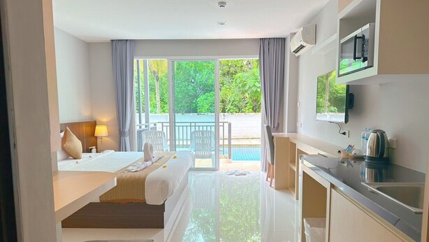 Une chambre d’hôtel moderne équipée d’un lit, d’un bureau, d’une kitchenette et d’un balcon avec vue sur la piscine.