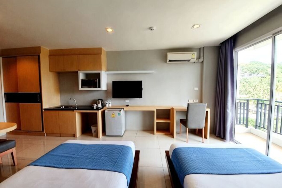 Une chambre d’hôtel avec une kitchenette, une télévision, un balcon et deux lits.