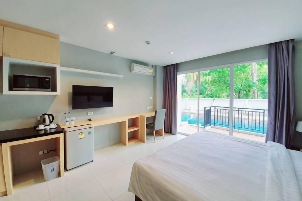 Ein Hotelzimmer mit einem Bett, einem Schreibtisch mit Fernseher, einem Minikühlschrank, einer Mikrowelle und Blick auf einen Swimmingpool.