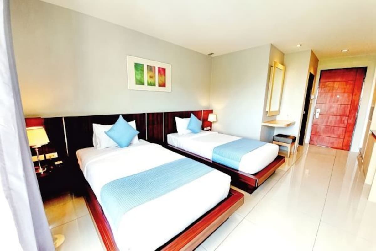Une chambre d’hôtel avec deux lits, une table de chevet, une commode, un miroir et une porte.