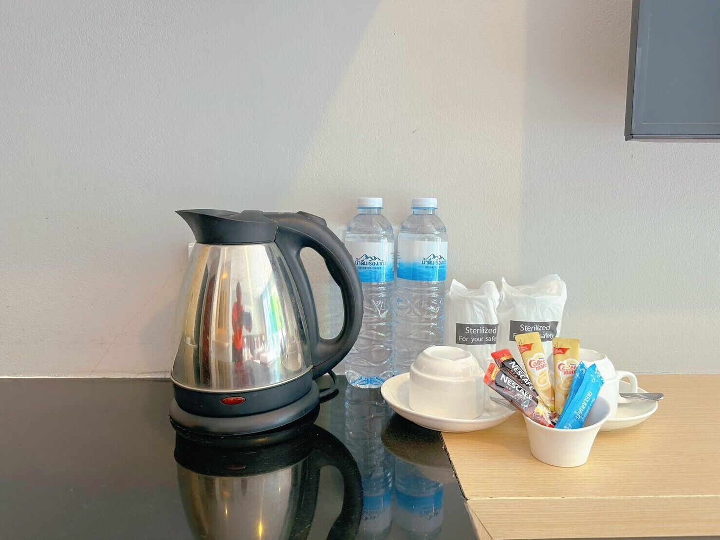 Een roestvrijstalen elektrische waterkoker, twee waterflessen, een kopje Nescafé en een kopje oploskoffie op een tafel.