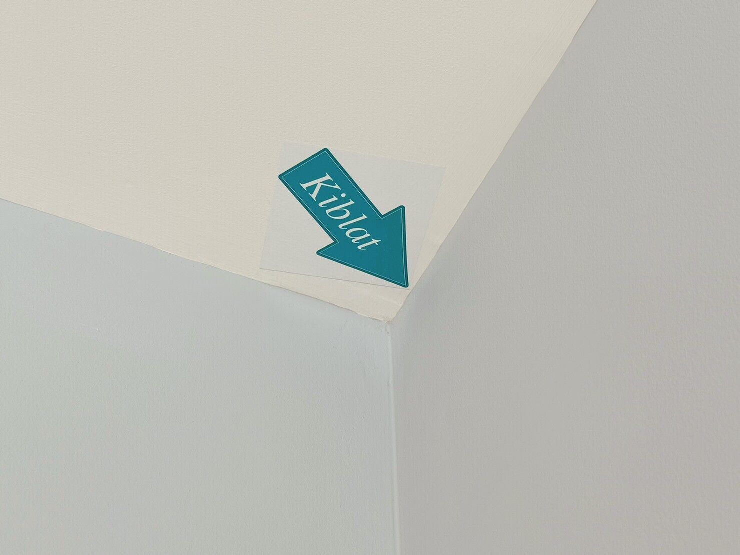 Une flèche indiquant la direction, avec le mot « Kibla » inscrit dessus, sur un mur blanc.