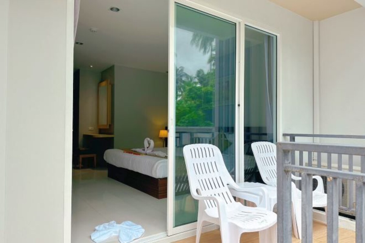 Une chambre d’hôtel avec un lit, une petite table et une chaise. Une porte-fenêtre coulissante donne sur un balcon équipé d’une chaise et d’une table.