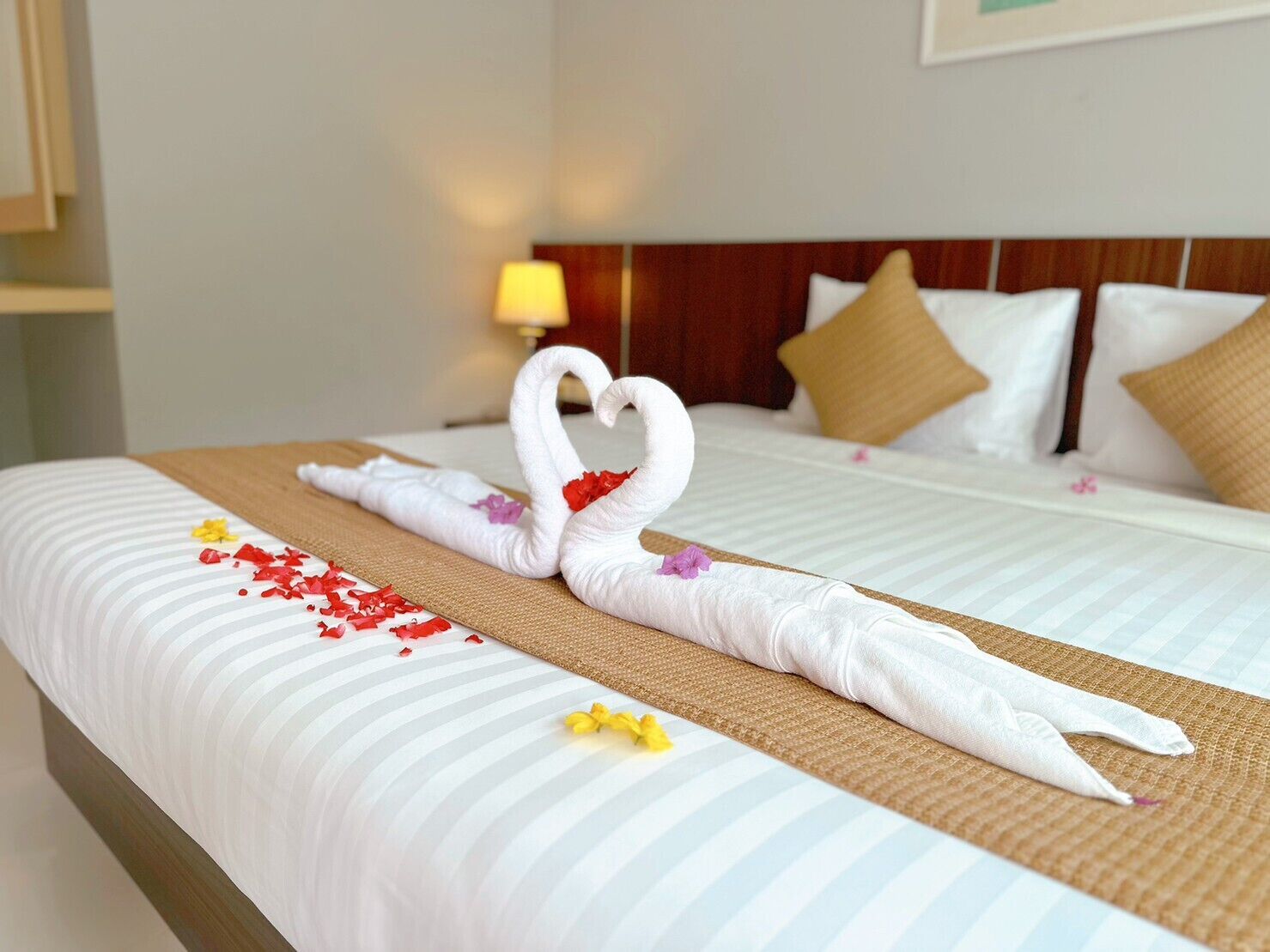 A hotel room with a neatly made bed, a wooden headboard, and a lamp on the nightstand.