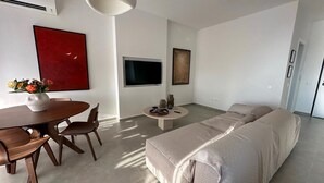 A modern living room with a beige sofa, a dining table with chairs, a TV, and artwork on the walls.